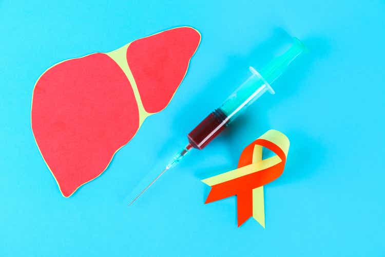 World Hepatitis Day. June 28th. Red yellow tape, a syringe with blood and a liver on a blue table.
