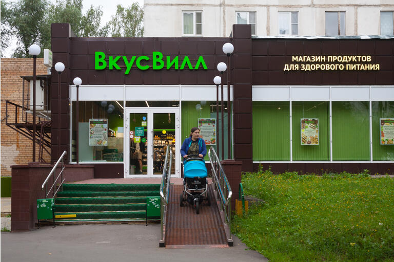 Food store building and woman with baby stroller 24.07.2018
