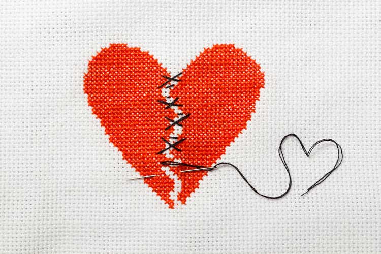 The broken heart is embroidered with red threads on a white cloth.