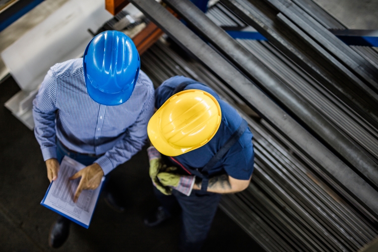 Above view of manager and manual worker reading reports in steel mill.