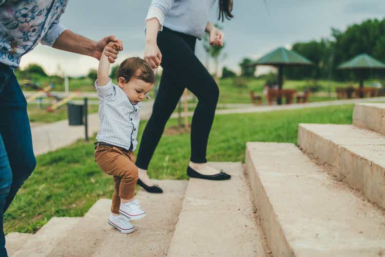 Baby walking with help of its parents - first steps