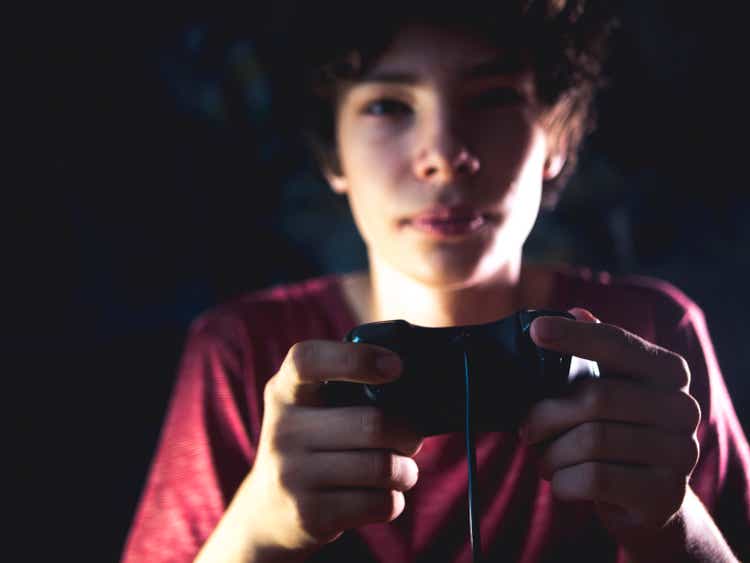 young teenager in dark bedroom playing console video game at night