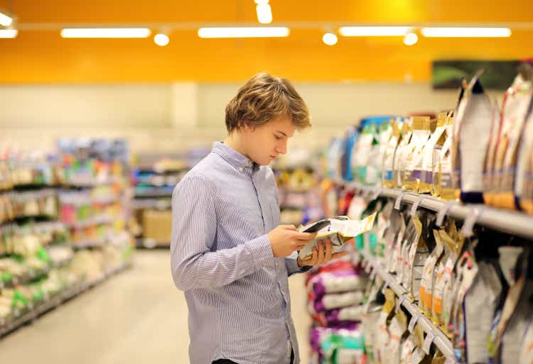 Man shopping in supermarket reading product information.Using smarthone.Pet food