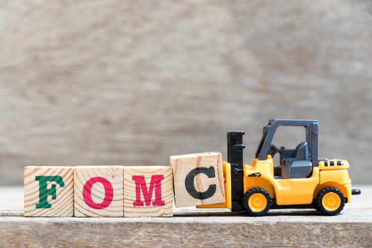 Toy forklift hold letter block c in word FOMC (abbreviation of Federal Open Market Committee) on wood background