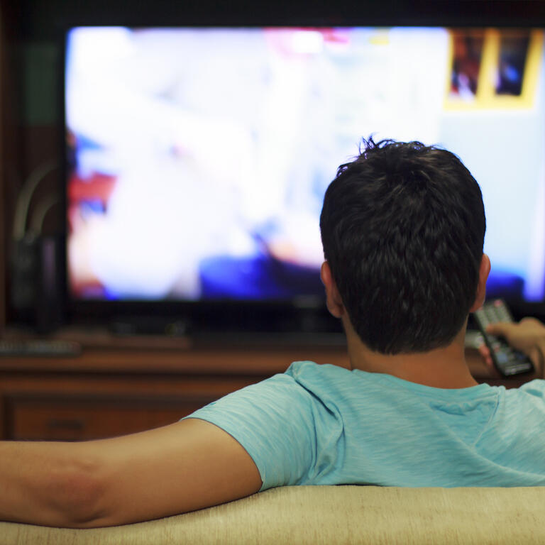 Male watching television in home living room / channel hopping