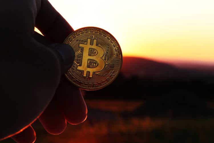 A golden bitcoin in his hand facing the sunset and the mountains in the distance