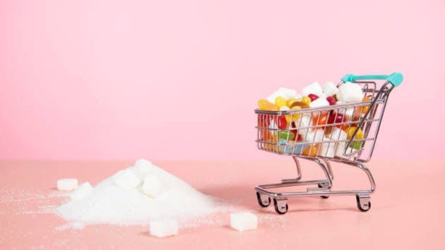 supermarket trolley with candy next to pile of sugar