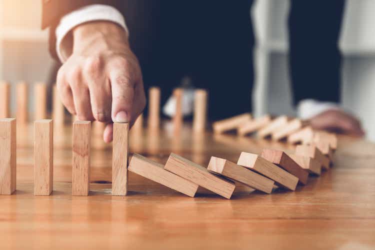 Close up finger businessman stopping wooden block from falling in the line of domino with risk concept.