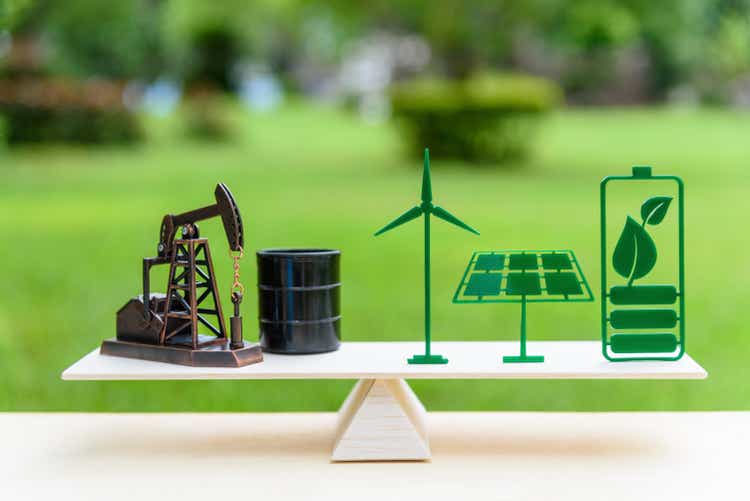 Fossil fuel vs renewable / future clean alternative energy concept : Petroleum pumpjack, crude oil drum barrel, solar panel, green leaf battery, wind turbine on a wood balance scale in equal position.