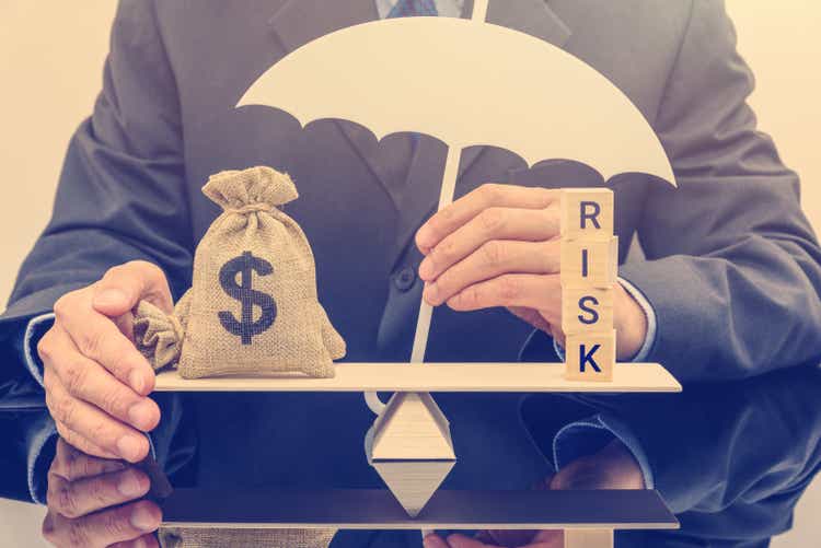 Financial risk assessment/portfolio risk management and protection concept: businessman holding white umbrella and protecting dollar bag on base balance scale, protecting money from deception or fraud