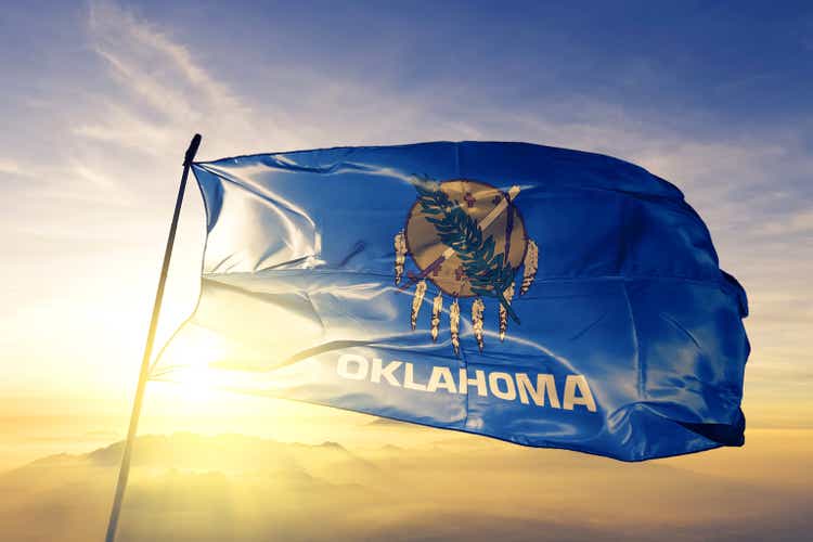 Oklahoma state of United States flag textile cloth fabric waving on the top sunrise mist fog