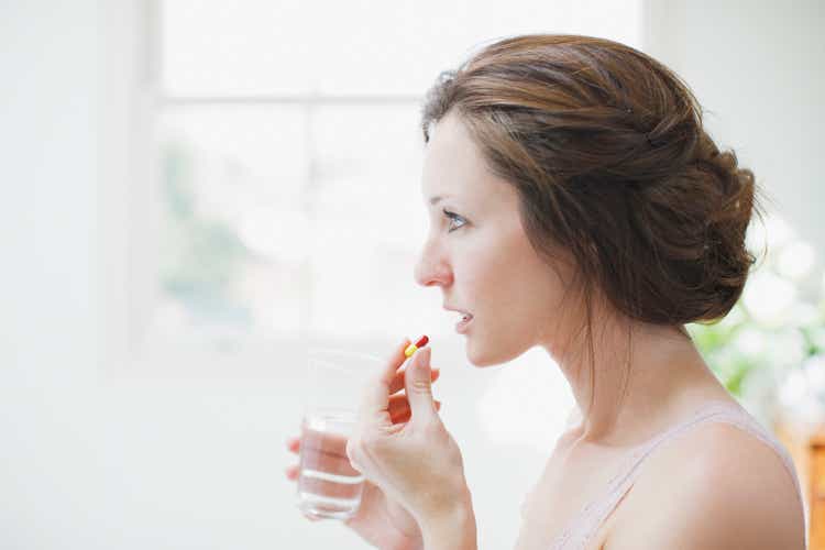 Woman holding glass of water and taking capsule