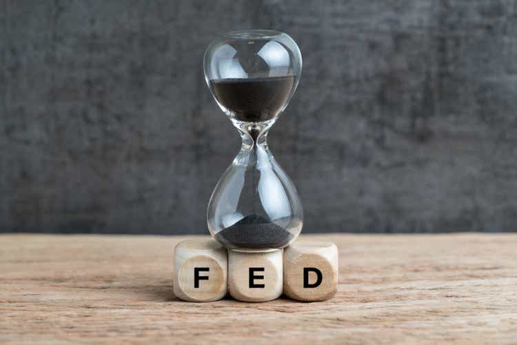 Federal Reserve, FED target and speed to raise interest rate concept, hourglass or sandglass on cube wooden block with alphabet building acronym FED on wooden table with dark background