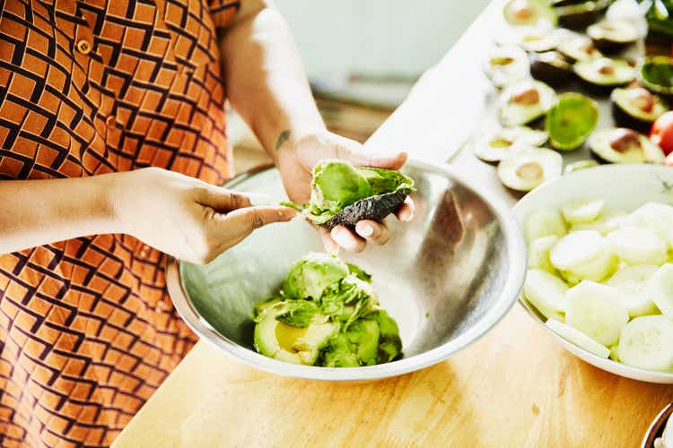 Woman scooping avocado into bowl while preparing food for party in kitchen