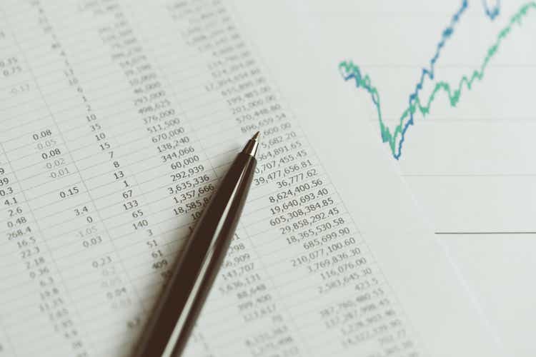 Investment, financial report statistic concept, close-up of black pen on printed stock exchange data price number or valuation table with green and blue yearly graph