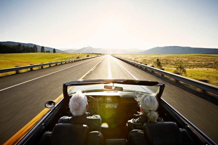 Senior couple driving convertible car at sunrise