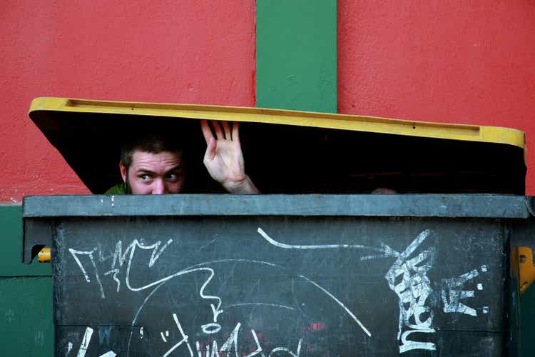 Young Man Hiding in Garbage Dumpster and Looking Out