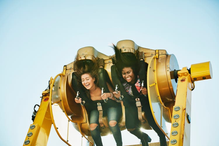 Laughing female friends spinning upside down on amusement park ride