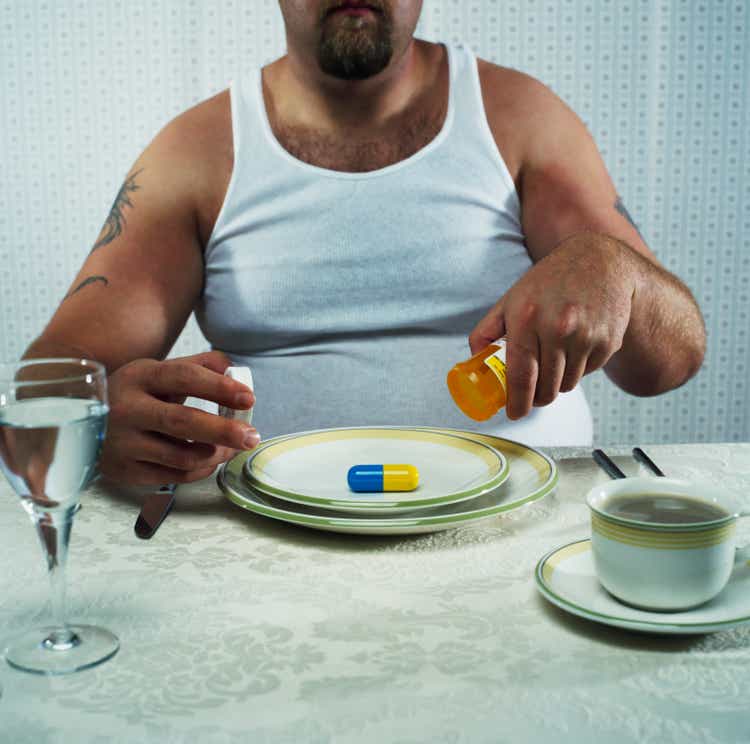 Overweight man emptying large pill from pill bottle