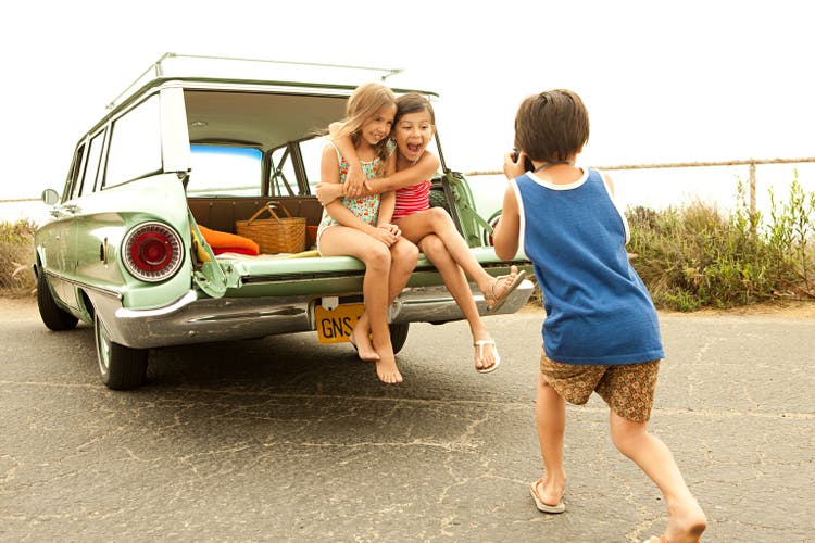 Three children sitting on back of estate car taking photographs