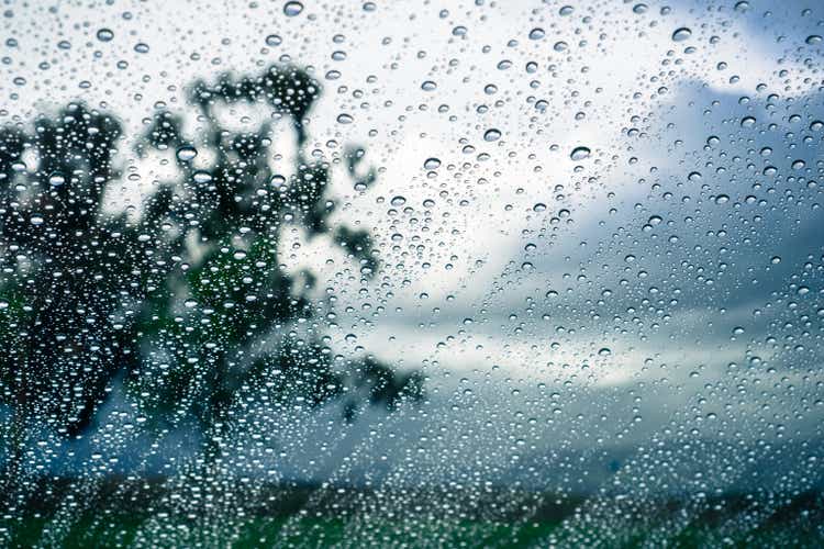 Drops of rain on the window; blurred trees and storm clouds in the background