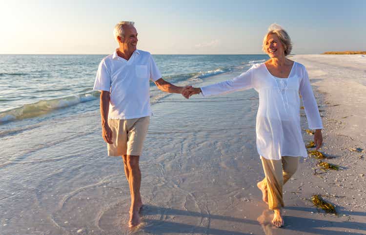 Happy senior man and woman couple walking and holding hands on a deserted tropical beach with bright clear blue sky