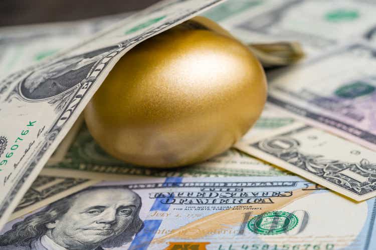 Shiny golden egg under pile of US America dollar banknotes money metaphor of finding the unbelievable good stock with high dividend or success investment in stock market concept