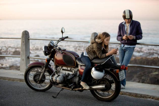 Father and daughter killing time on cellphones around motorcycle