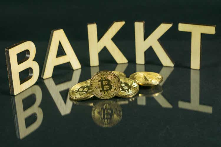 Bitcoin coins in front of bakkt sign made of wood with reflection on the table, Slovenia - December 27th