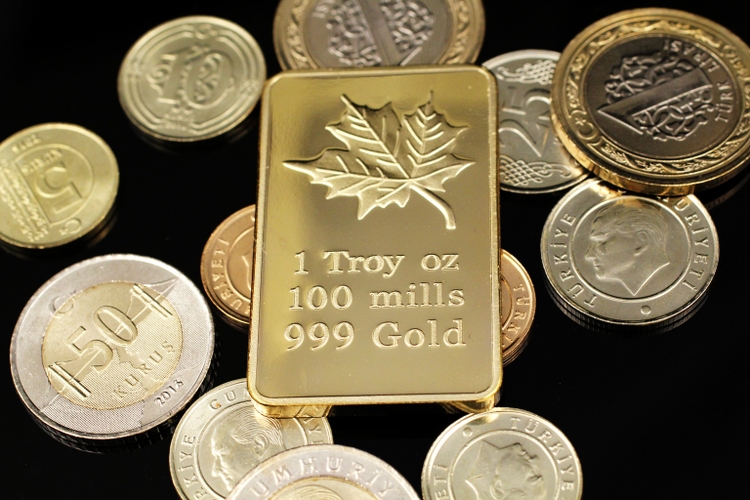 A close up image of Turkish coins and a gold Canadian one ounce ingot on a black background