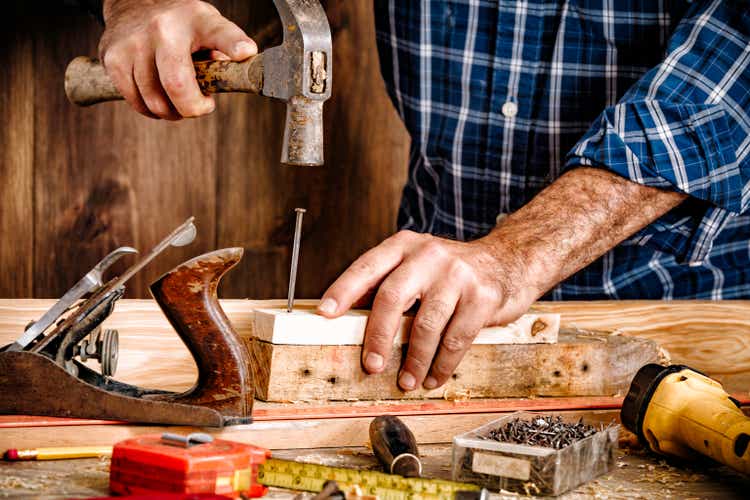 Hammer nail and hands close up shot on lumber plank in home workshop