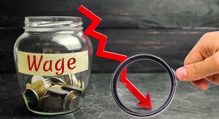 Glass jar with coins and the word Wage and a red down arrow. Salary reduction. Drop in profits. Financial crisis. Demotion. Low profit. Capital outflow. Concept of business and finance