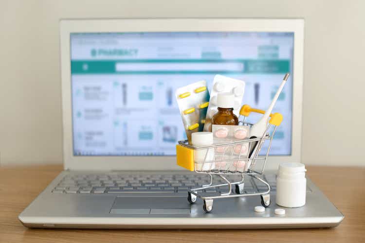 Shopping cart toy with medicaments in front of laptop screen with pharmacy web site on it. Pills, blister packs, medical bottles, thermometer set. Health care and internet shopping.