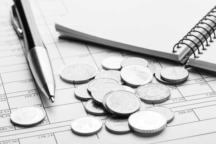 Stack of euro euro coins on old black wooden table. Pen, notebook and accounting documents with numbers