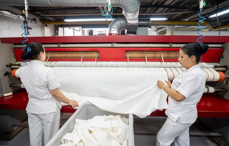 Women working at a laundry service ironing sheets using an industrial iron
