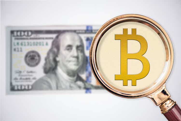 Bitcoin icon instead of hundred dollars under magnifying glass.  concept of major international currency