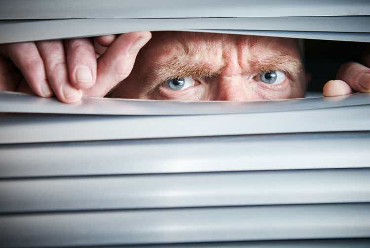 Man peers through closed blinds, looking worried