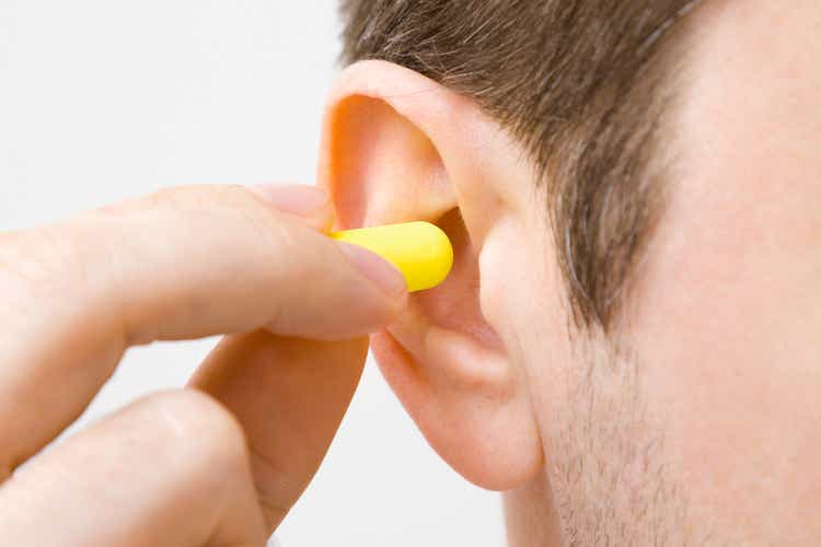 Young man"s fingers putting yellow earplug into his ear on light gray background. Closeup.