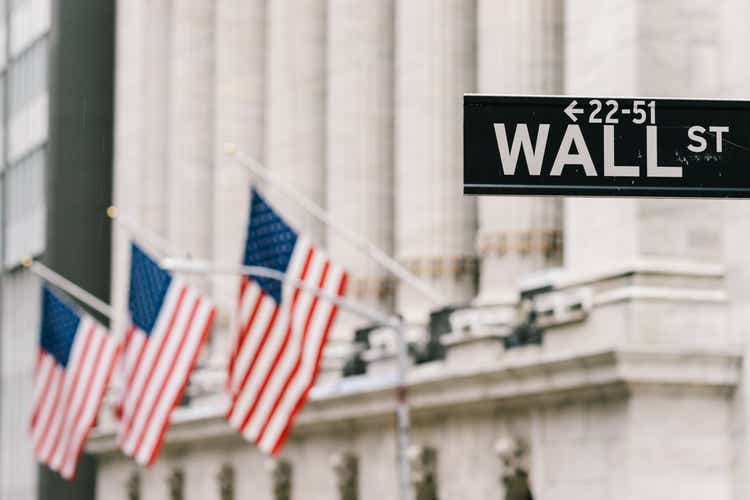 Wall Street sign post with American national flags in background. New York city financial district, stock market trade and exchange, or business concept