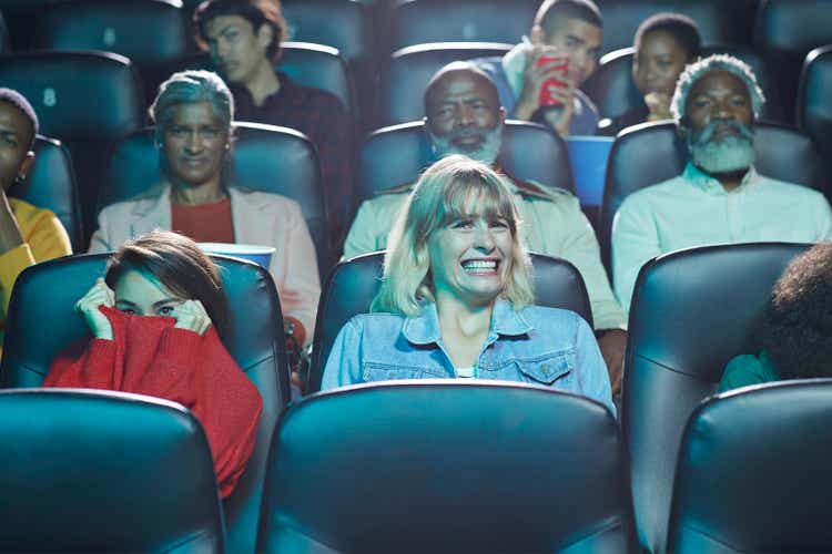 Frightened multi-ethnic men and women watching horror movie in cinema hall of theater