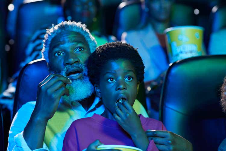 Shocked father and daughter eating popcorn while watching horror movie in theater