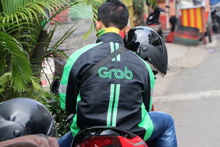 Behind the man sitting on the motorcycles beside the road who is a Grab bike in Indonesia.