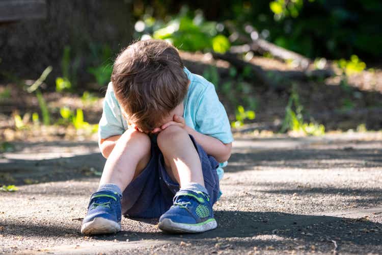 Crying toddler sitting on the floor covering his face