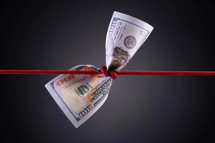 Amerikanischer Dollar in rotem Seil Knoten auf dunklem Hintergrund mit Kopierraum gebunden. Unternehmensfinanzen, Spar- und Konkurskonzept.