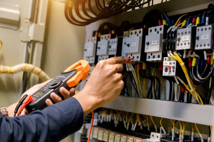 Electrician engineer work tester measuring voltage and current of power electric line in electical cabinet control.