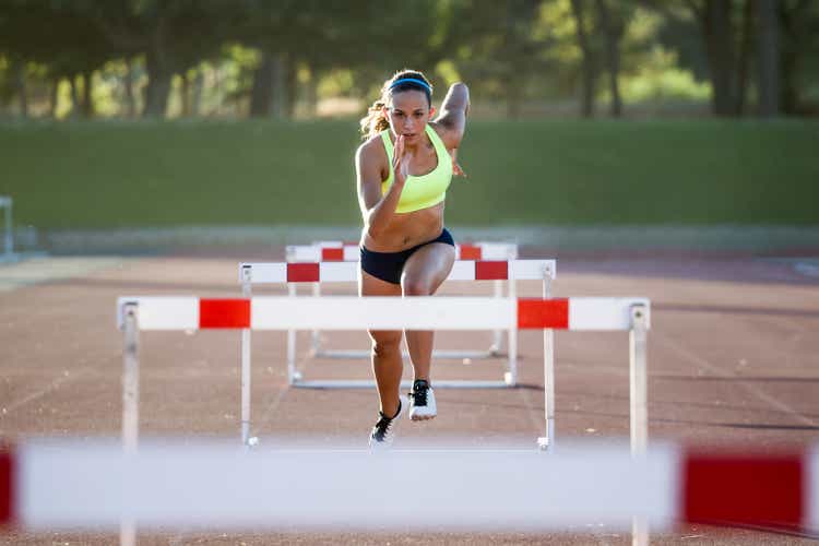Young athlete jumping over a hurdle during training on race track.