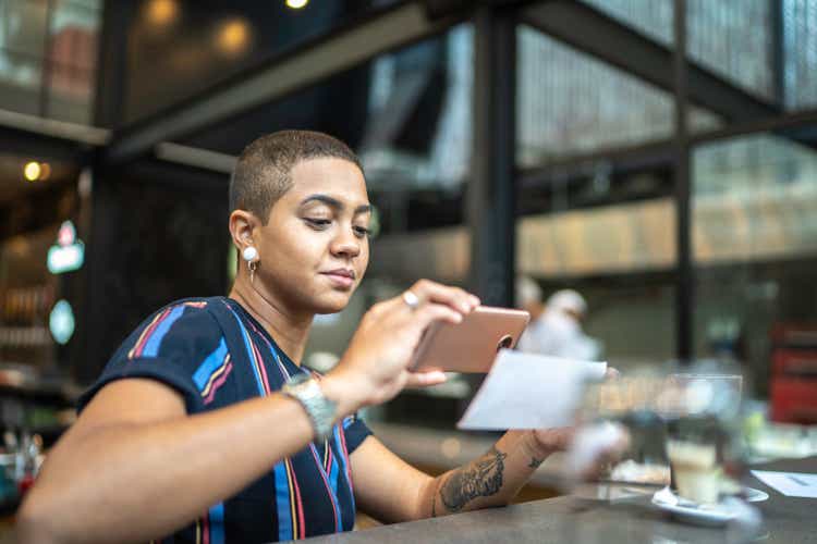 Young woman depositing check by phone in the cafe