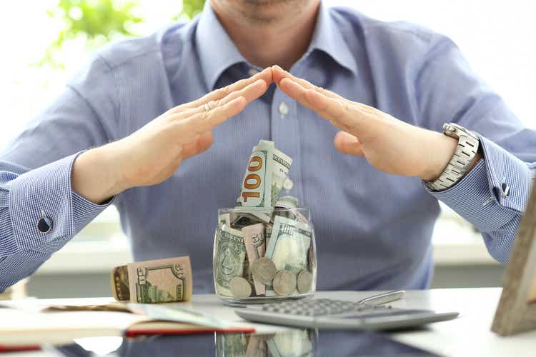 Defend Your Investments: 2 High-Yielding Preferred Stocks for Consistent Income 1 Male hands defending big jar full of US currency as solidity and reliability symbol