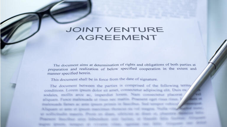 Joint venture agreement lying on table, pen and eyeglasses on official document