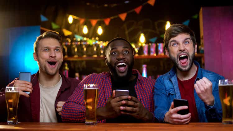 Multiethnic friends supporting favorite team, making bets for game result in pub
